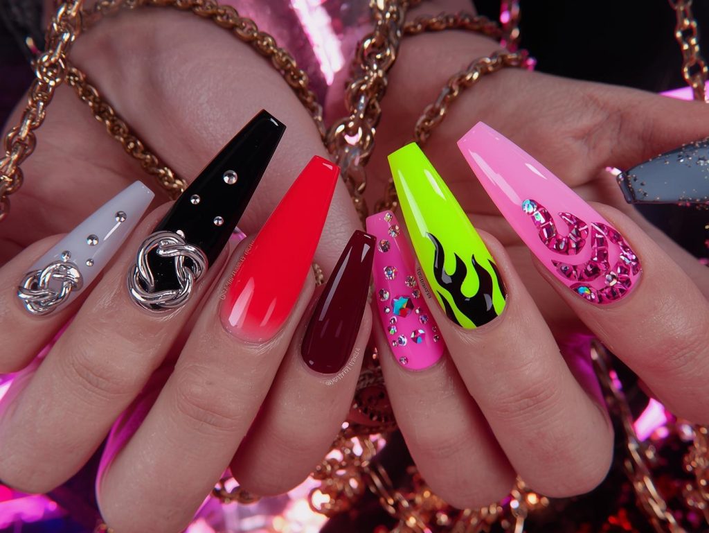 Baddie nail designs with chrome silver chains, gold stud embellishments, black flame patterns, and holographic rhinestone details for captivating Pinterest inspiration.