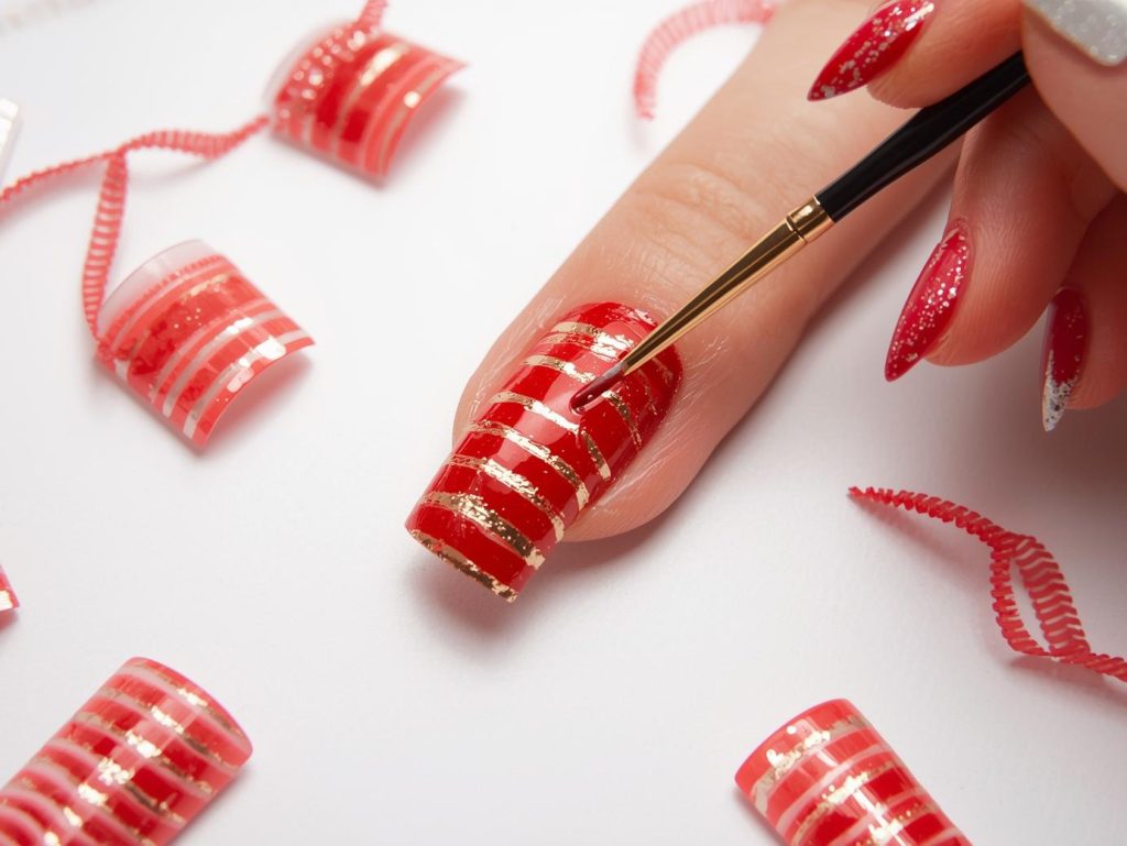 Creating vibrant red gold striped nail art with gold horizontal stripe patterns.