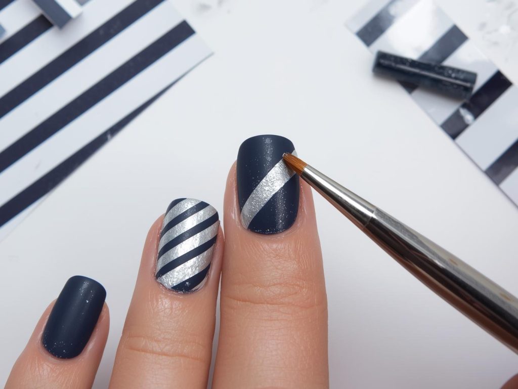 Creating matte navy silver striped nail art with silver diagonal stripe patterns.