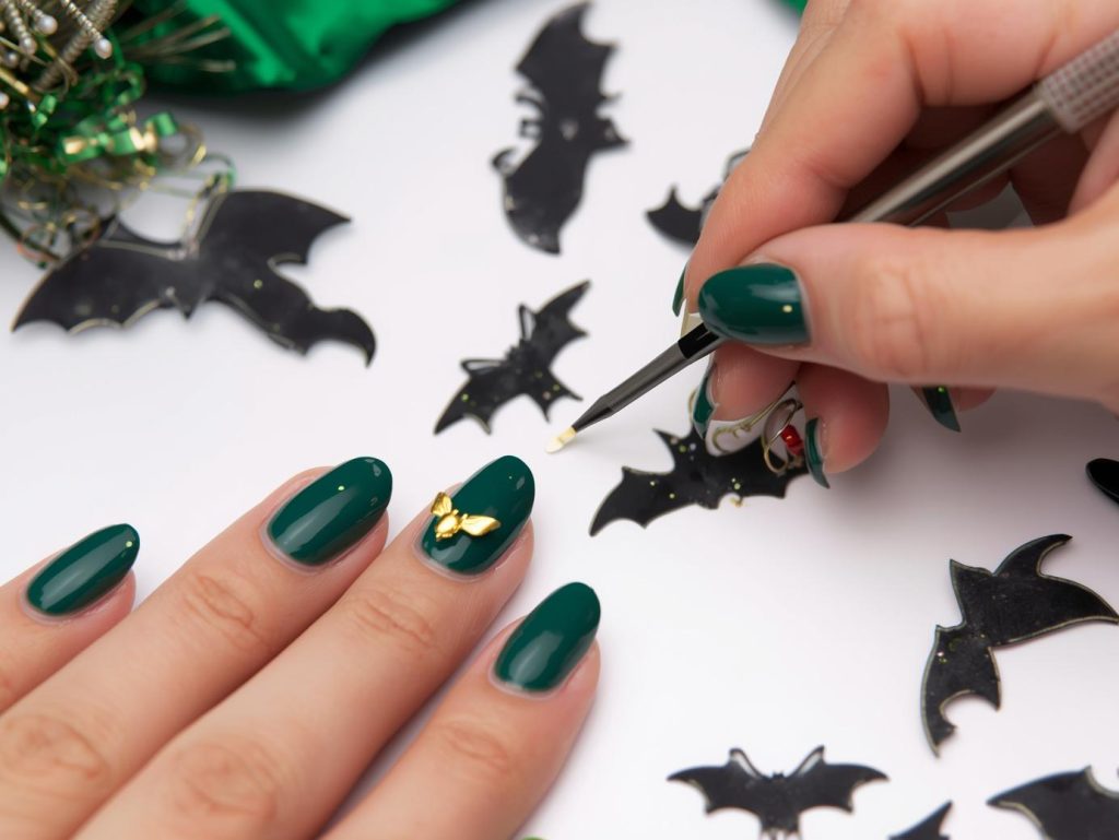 Applying deep green gold bat Kiss Halloween nail design with gold accents.