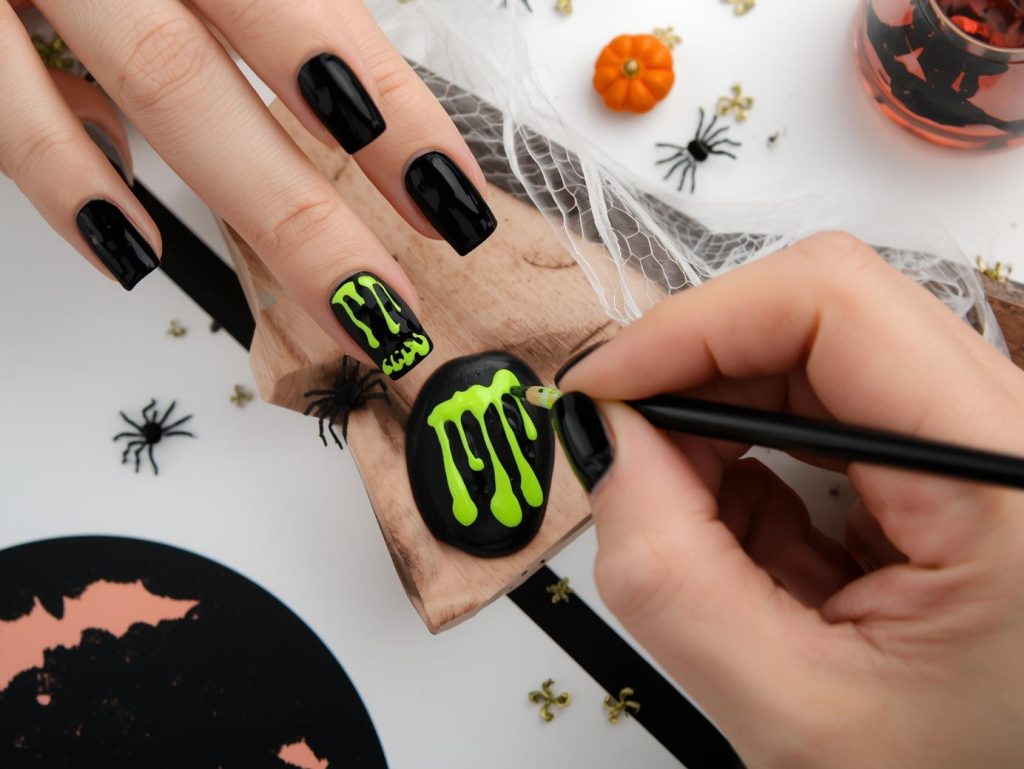 Applying glossy jet black slime drip Halloween nail inspo with neon green drips.