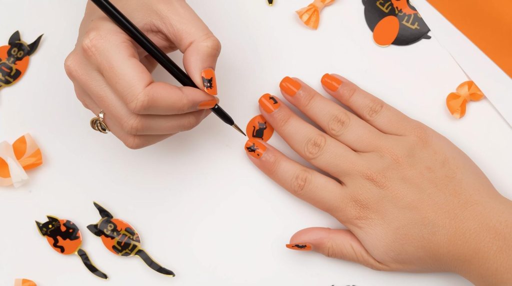 Cute Halloween Nails: Adorable and Pinterest-Worthy Manicures to Adore 6 Applying glossy orange black cat cute Halloween nail design with black cat decals.