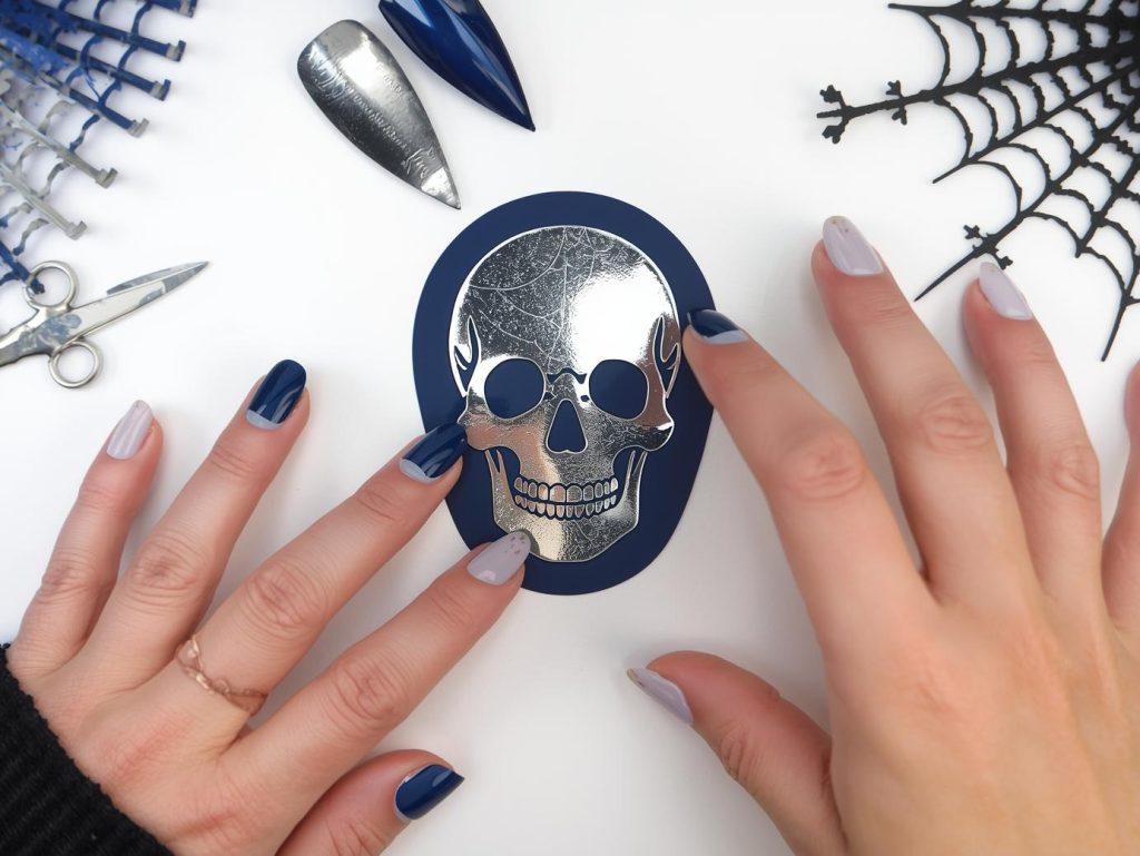 Applying glossy midnight blue skull sticker short Halloween nail design with silver stickers.