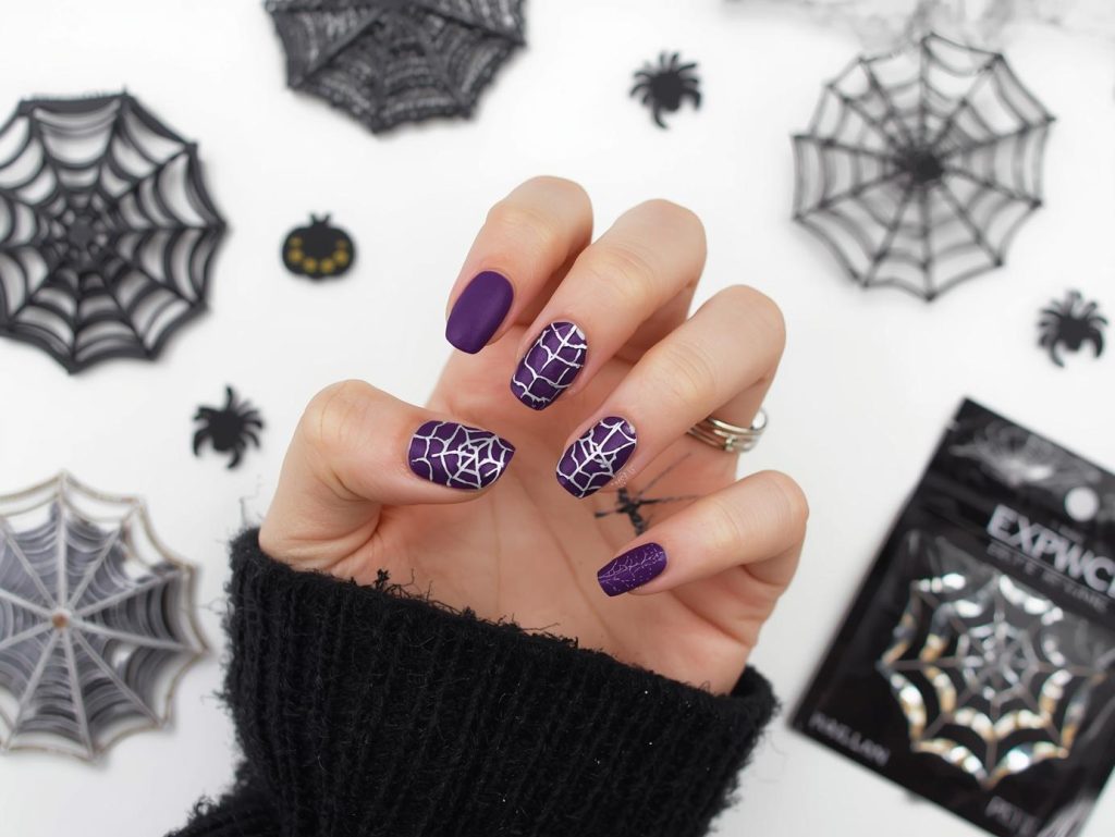 Applying matte purple silver spider web Halloween press-on nails with silver decals.